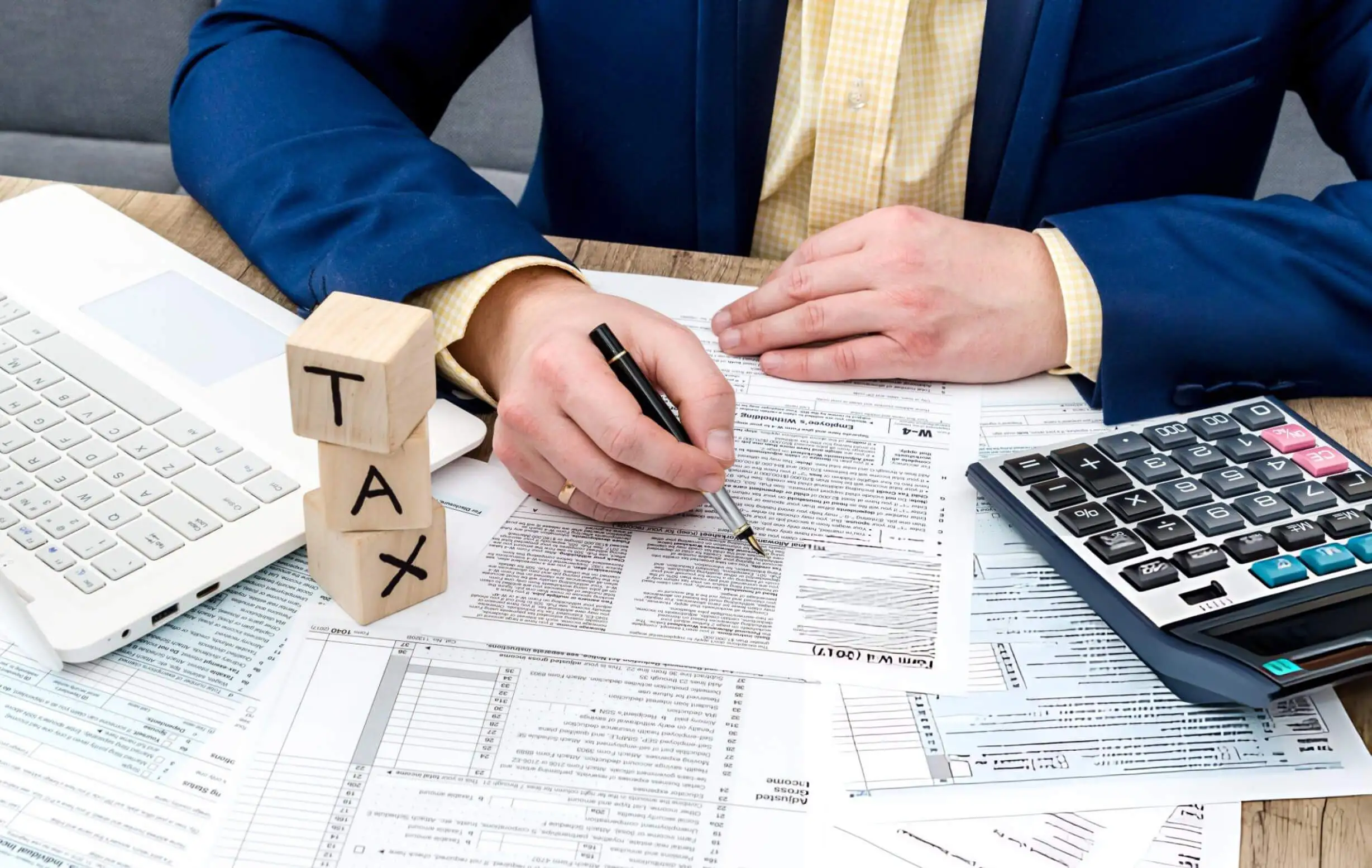 Businessman filling W-4 form with pen, calculator and pc